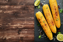 Grilled Corn With Lime Pieces And Seasonings On Wooden Table