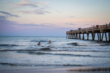People Surfing By Pier In The Sunset