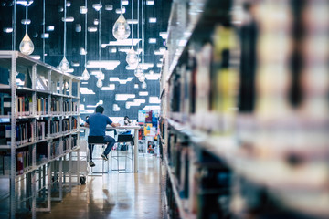 People studying in public modern library - man sitting viewed from back working at computer laptop - city space for students to learn and teach - defocused book - focus on male in background