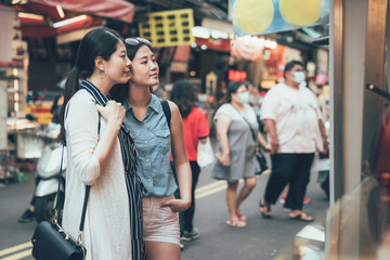 Wall Mural - Happy women tourists standing on road street looking at food vendor cart outdoors in local market. two young girls travelers together waiting for order meal. trip in japan downtown lifestyle taiwan