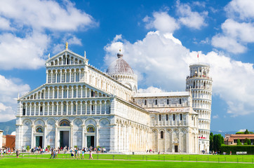 Pisa Cathedral Duomo Cattedrale and Leaning Tower Torre on Piazza del Miracoli square green grass lawn, blue sky with white clouds background in sunny day, Tuscany, Italy