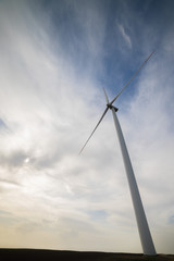 One wind turbine on agricultural ground with cloudy sky in background