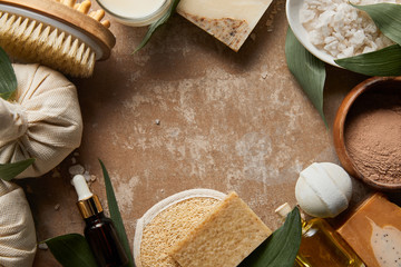 top view of natural cosmetics and beauty supplies on textured weathered beige surface with green leaves