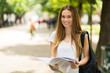 © Minerva Studio - Female student holding a book outdoor in the park and smiling