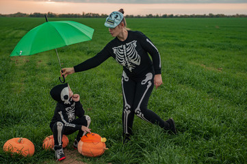 Girl mother with children in skeleton bone on green field with umbrella with pumpkins on eve of  holiday Halloween