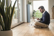 © Westend61 - Young man sitting cross-legged in front of window, using laptop