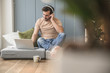 © Westend61 - Young man sitting on mattress, using laptop with headphones
