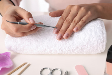 Woman preparing fingernail cuticles at table, closeup. At-home manicure