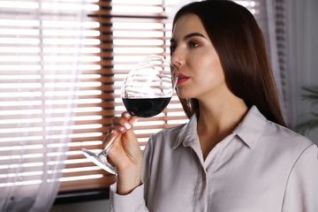 Beautiful young woman with glass of luxury red wine indoors. Space for text