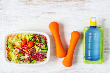 Wall Mural - Fresh vegetable salad in lunch box with orange dumbbells excercise equipment and energy water drink on white rusty wood background. Active healthy lifestyles, good health Concept. 