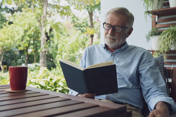 senior man happiness sitting and reading book at balcony near garden at nursing home for relaxing