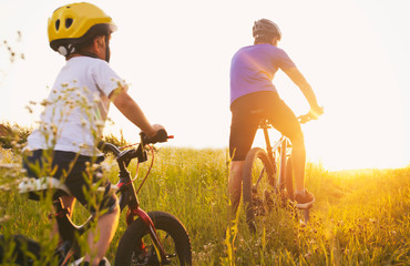 Father and son together are riding bicycles through the pathway in the field