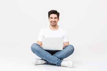 Wall Mural - Excited young man posing isolated over white wall using laptop computer.