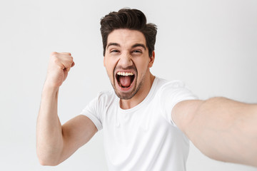 Poster - Excited happy young man posing isolated over white wall background make a selfie by camera.