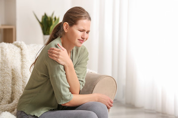 Wall Mural - Young woman suffering from pain in shoulder at home