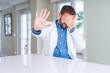 © Krakenimages.com - Handsome doctor man wearing medical coat at the clinic covering eyes with hands and doing stop gesture with sad and fear expression. Embarrassed and negative concept.