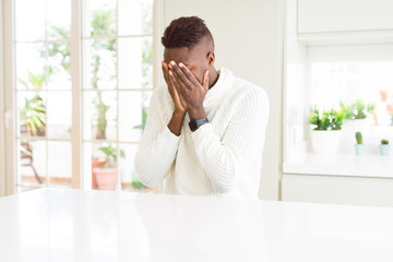 Poster - Handsome african american man on white table with sad expression covering face with hands while crying. Depression concept.