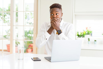 Poster - African american business man working using laptop shocked covering mouth with hands for mistake. Secret concept.