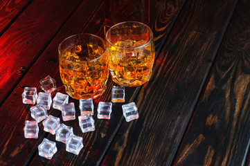 Wall Mural - Two glasses of whiskey with ice cubes served on wooden planks.