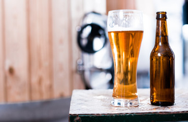 bottle and glass with gold beer on the background of barrels for fermentation