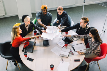 Wall Mural - Top view of multiracial young creative people in modern office. Group of young business people are working together with laptop, tablet, smart phone, notebook. Successful hipster team in coworking.