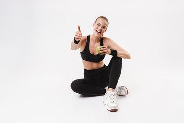 Sticker - Image of pretty smiling woman wearing tracksuit sitting on floor with thumb up and green apple