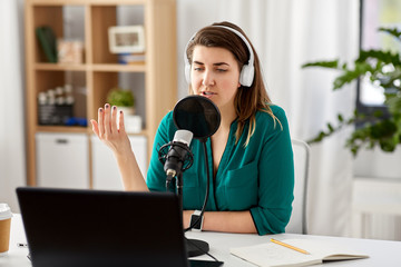 Wall Mural - technology, mass media and people concept - woman in headphones with microphone and laptop computer talking and recording podcast at studio