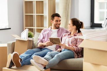 Wall Mural - moving, people, repair and real estate concept - happy couple with photo frame and cardboard boxes sitting on sofa at new home