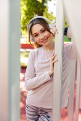 Poster - Beautiful cheerful young fitness sports woman posing outdoors in park listening music with earphones.