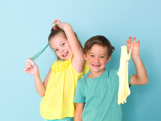 cool, pretty boy and his older sister are playing with homemade slime in front of a blue background and having a lot of fun and are laughing