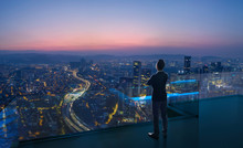 Businessman Standing On Open Roof Top Balcony Watching City Night View . Business Ambition And Vision Concept .