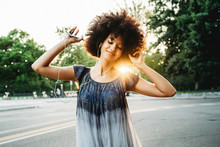 Young Black Woman Dancing Listening To The Music With Earphones From The Smart Phone Outside A Park At Sunset On A Summer Day