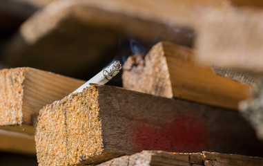 Burning cigarette on pine wood boards, conceptual human negligence image close up macro shot.