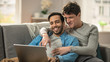 © Gorodenkoff - Sweet Male Queer Couple Spend Time at Home. They are Lying Down on a Sofa and Use the Laptop. They Browse Online. Partner's Hand is Around His Lover. They Smile and Laugh. Room Has Modern Interior.