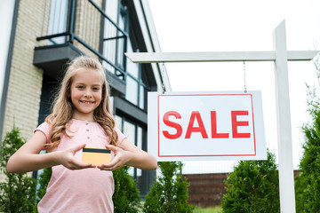 Wall Mural - low angle view of happy kid holding credit card near board with sold letters