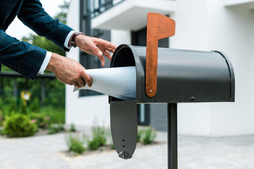 cropped view of man putting blank paper in mail box near house