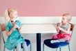 Lifestyle portrait of two happy Caucasian cute adorable funny children girls sitting together bragging boasting their ice-cream. Love envy jealous sisters friendship. Tasty yummy summer food