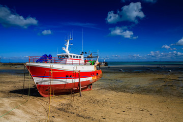 Red and white fishing boat under maintenance out of water on the sands 