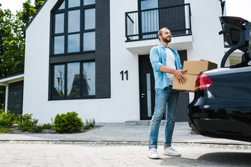 Wall Mural - happy man holding boxes near car and modern house