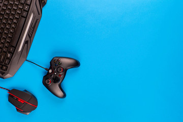 A keyboard and a mouse next to a controller on blue background, shot from above.