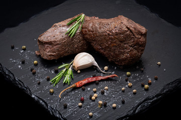 Wall Mural - Grass Fed Corn Roast Beef garnished with Fresh Rosemary, dried Red Chile Pepper, Garlic and Rainbow  Peppercorns on natural black stone background.