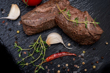 Wall Mural - Grass Fed Corn Roast Beef garnished with Tomatoes, Fresh Thyme, dried Red Chile Pepper, Garlic and Peppercorns on natural black stone background.