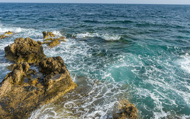 Travel, Summer cliff next to the Mediterranean Sea, strong waves break with the rocks and leave blue and turquoise colors along with the foam of the sea.