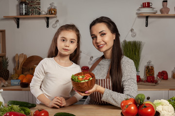 Mother and her daughter are making a vegetable salad and having fun at the kitchen.