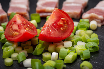 Wall Mural - Uncured Apple Smoked Bacon, Red Tomatoes and Green Onion Scallions  arranged on black natural stone background.