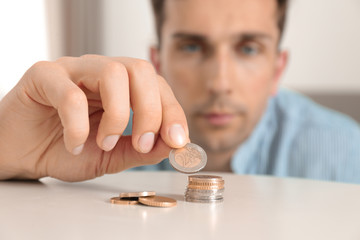 Young man stacking coins at table, focus on hand