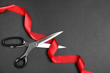 stylish scissors and red ribbon on black background, flat lay with space for text. ceremonial tape c