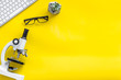 Leinwandbild Motiv Do medical research on laboratory desk with microscope, keyboard, glasses on yellow background top view mockup