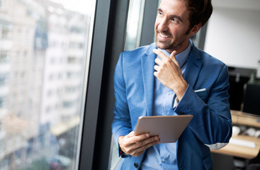 Portrait of young businessman smiling while using digital tablet in office