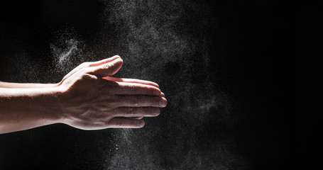 Powdery flour flying into air as man in black chef outfit wipes off his hands